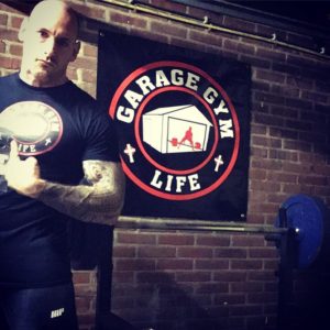 Tim Geurts posing in front of a Garage Gym Life Logo Wall poster