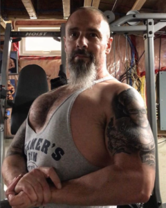 Heart attack survivor Rich Dlin hits a side chest pose in his basement gym